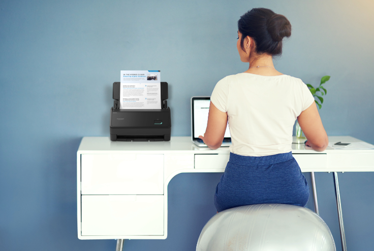 A woman sat at a desk working with an iX2400 black scanner beside her